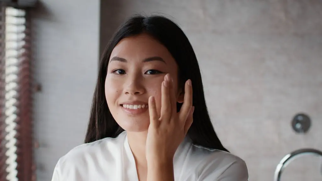 happy-korean-woman-applying-facial-cream-moisturizing-skin-in-bathroom-SBI-350188977 | Contour Dermatology woman with clear skin