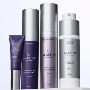 Lineup of Alastin skincare products in purple and silver packaging on a shelf, including serums and a tube badge.