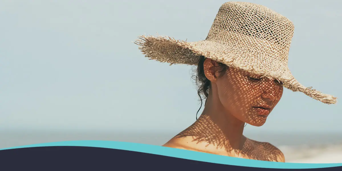 01-Desert-Skincare-Routine | Contour Dermatology Woman wearing a wide-brimmed straw hat at the beach, shadows from the hat pattern her face and shoulders.