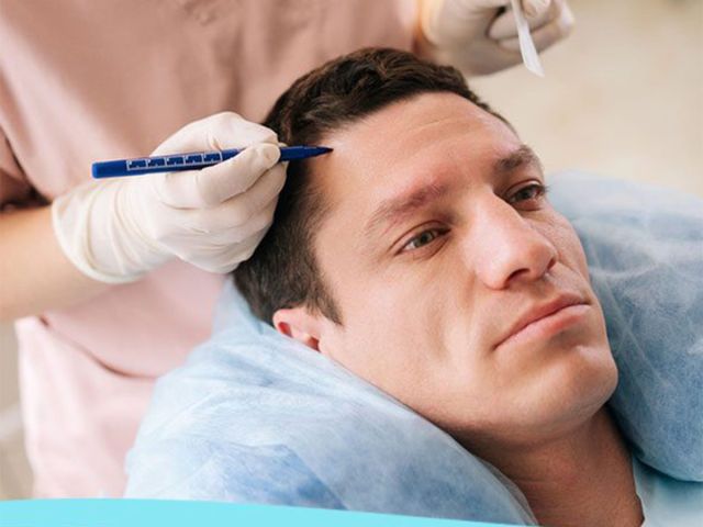 Man lying back as a clinician performs an eyebrow procedure with a gloved hand and a precision tool near his brow.