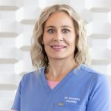 Smiling healthcare professional in blue scrubs facing the camera; name badge reads 'Dr. Jochen's Favorite'.